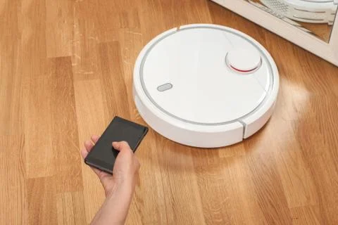 Womens hand using mobile to control white robotic vacuum cleaner. modern smar Stock Photos