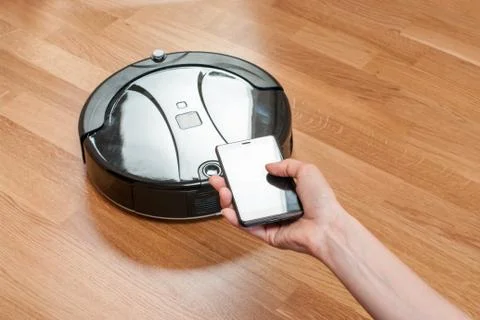 Womens hand using mobile to control black robotic vacuum cleaner. modern smar Stock Photos