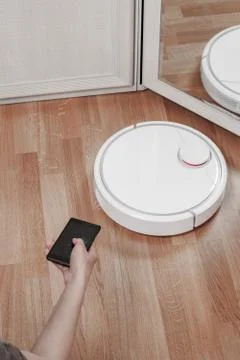 Womens hand using mobile to control white robotic vacuum cleaner. modern smar Foto stock
