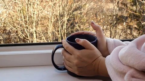 Women's hands are holding a big blue cup with hot tea in the open window Stock Footage 82715843