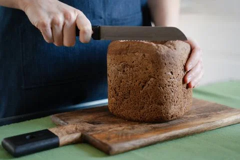Women's hands begin to cut with a knife a loaf of homemade black dark Darnits Stock Photos