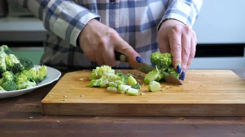 Women's hands cut broccoli on a cutting board with a knife. Then he puts it on a Stock Footage 167559197