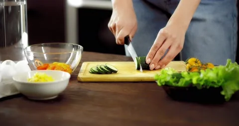 Women's hands cut a cucumber with a knife on a cutting board. Stock Footage 182345899