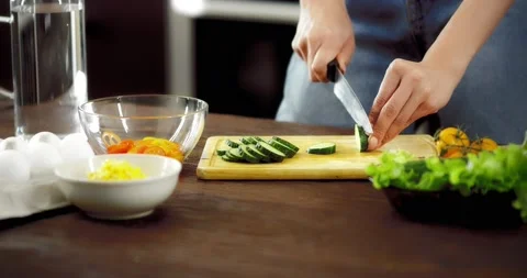 Women's hands cut a cucumber with a knife on a cutting board. Stock Footage 182349803
