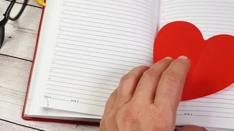 Women's hands flip through the pages of the diary and take out two red hearts, 스톡 동영상 146778196