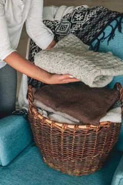 Women's hands fold a stack of warm knitted sweaters in wicker b Stock Photos