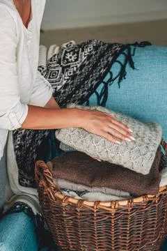 Women's hands fold a stack of warm knitted sweaters in wicker b Stock Photos