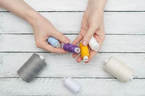 Women's hands hold colored thread for sewing on wooden white boards Stock Photos