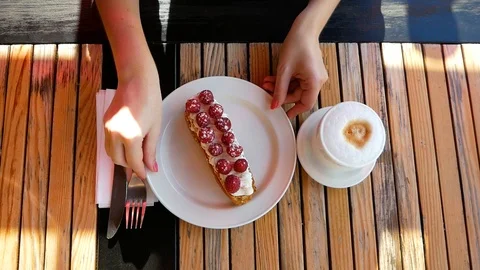 Women's hands hold a plate with raspberry dessert. A cup of latte is standing Video stock 100036224