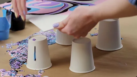Women's hands hold a sheet of paper with multi-colored paint poured on it. Stock Footage 194998651