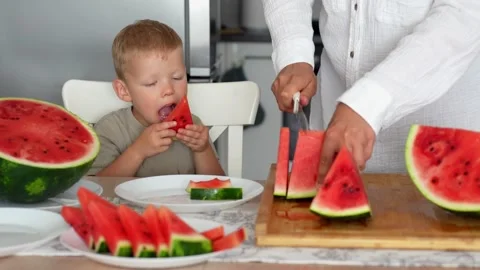 Women's hands in the kitchen cut a ripe watermelon into triangular slices Stock Footage 290982176