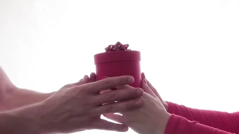 Women's hands pass red gift box on white background, masculine hands take box 動画素材 131436662