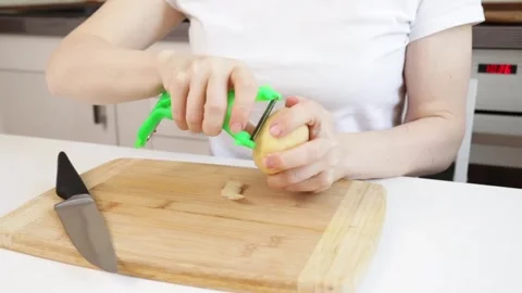 Women's hands  peeling potatoes with a vegetable peeler in the kitchen, pre.. Stock Footage 308703591