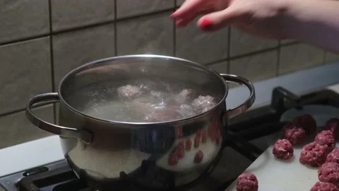 Women's hands put meatballs in boiling water. Soup preparation process. Close-up Stock Footage 154998016