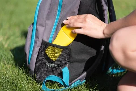Women's hands put sunscreen in a backpack on the green grass background. Stock Photos