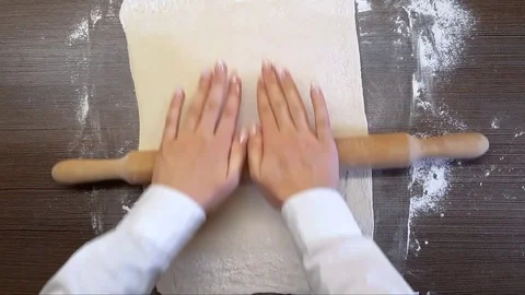 Women's hands roll out the dough with a wooden rolling pin, on the surface of Stock Footage 128540309