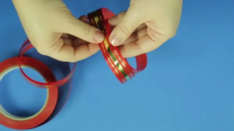 Women's hands shape the blank for a red ribbon gift bow. Blue background. Stock Footage 98417945
