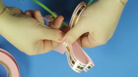 Women's hands shape the petals of a pink ribbon gift bow. Blue background. Stock Footage 98947220