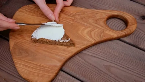 Women's hands spread white cheese on bread lying on a cutting board. Sandwich Stock Footage 150333276