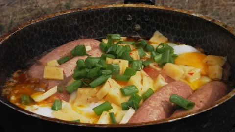 Women's hands sprinkle eggs with green onions in a frying pan with tomatoes Stock Footage 203240057