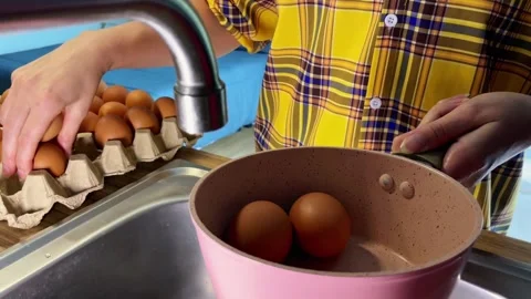Women's hands transfer chicken eggs into a saucepan and add water before boiling Stock Footage 338076745
