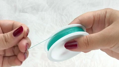 Womens hands unwrap plastic wire for beading. Elastic blue wire. Видео 314308522