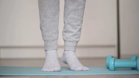 Women's legs in gray sweatpants do foot stretch on the mat. Home exercise Stock Footage 153202702