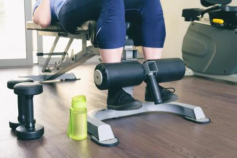 Women's legs on the simulator during a workout, next to a bottle of water a.. Stock Photos