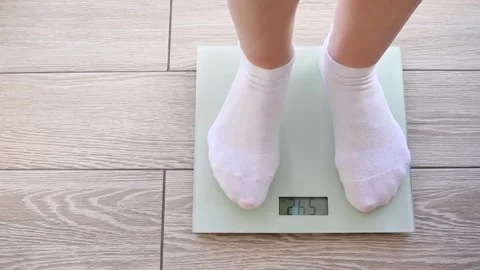 Women's legs in white socks step on the floor scales. 54 kg Stock Footage 258418447
