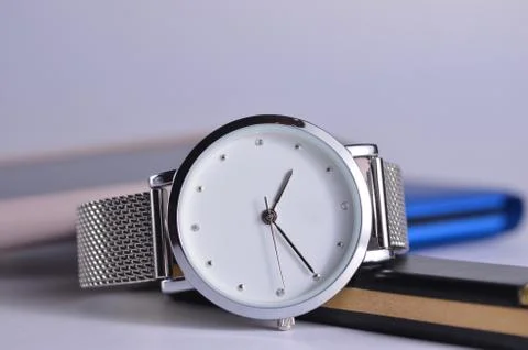 Women's watch with a silver strap on the table. Phone, notepad and flash drive o Stock Photos