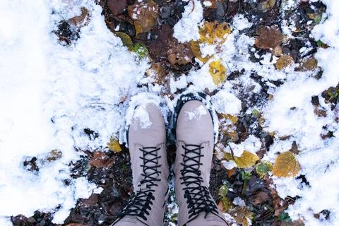 Women's winter boots with laces on a path covered with autumn leaves and whit Stock Photos