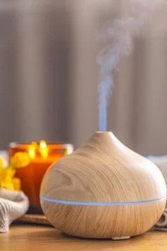 Wood aroma diffuser producing mist with candle and flowers in cozy spa inte.. Stock Photos