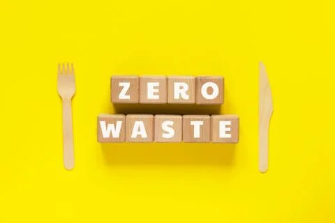 Wood cubes with text ZERO WASTE, wooden fork and knife on yellow background. Foto stock