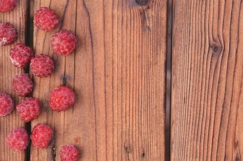 On a wooden background, raspberry is spread out on the left Stock Photos