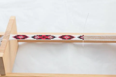 Wooden beadwork machine with strained threads and part of ready beaded necklace Foto stock