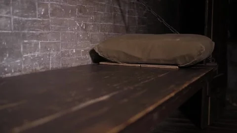 A wooden bed hanging on chains, a shelf with a pillow in an old prison cell. Stock Footage 310656426