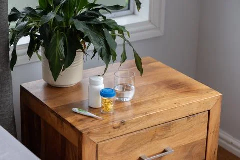 Wooden bedside table sitting by window in bedroom, holding plant, pill bottles, Stock Photos