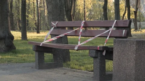 Wooden bench in empty park behind restrictive red white tape Stock Footage 129240567
