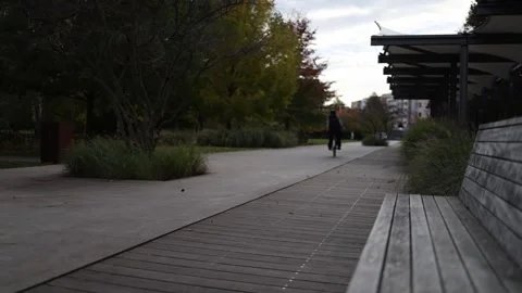 Wooden bench in focus with blurred background of park path and cyclist passing b Stock Footage 319841941