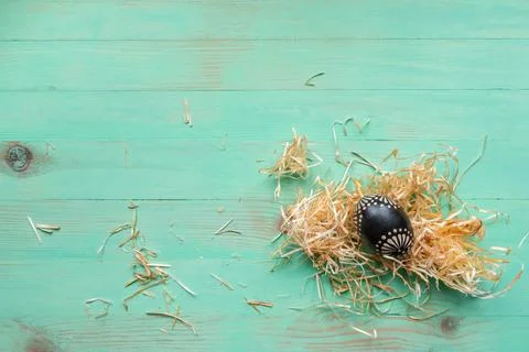 Wooden black painted patterned Easter egg and hay straws around on wood backg Stock Photos