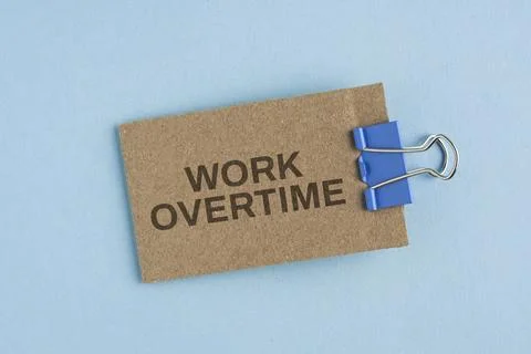 Wooden blocks labeled WORK OVERTIME, pinned against a blue background, symb.. Stock Photos