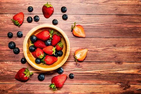 A wooden bowl with strawberries and blueberries on a wooden table.  Stock Photos