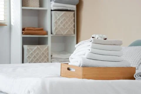Wooden box with stack of towels and cotton flowers on bed in room Stock Photos