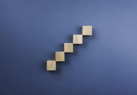 Wooden cube blocks stacking as a chart step stair on a blue background, top v Foto stock