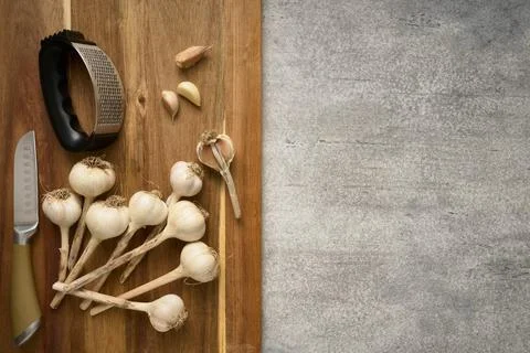 Wooden cutting board with garlic heads and garlic press, close up Stock Photos