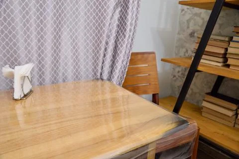Wooden dining table with protective plastic cover and chair near patterned .. Stock Photos