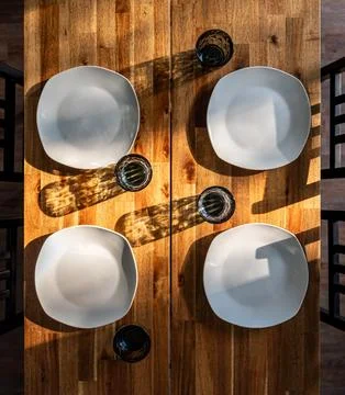 Wooden dining table set for four. Sunlit tableware and dining scene. Stock-Fotos