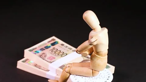 A wooden doll sitting on a chair with a stack of bills, rotating Stock Footage 312533259