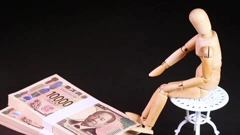 A wooden doll sitting on a chair with stack of bills rotating Stock Footage 313413383