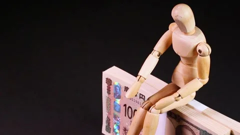 Wooden doll sitting on a stack of bills, rotating Stock Footage 313815553